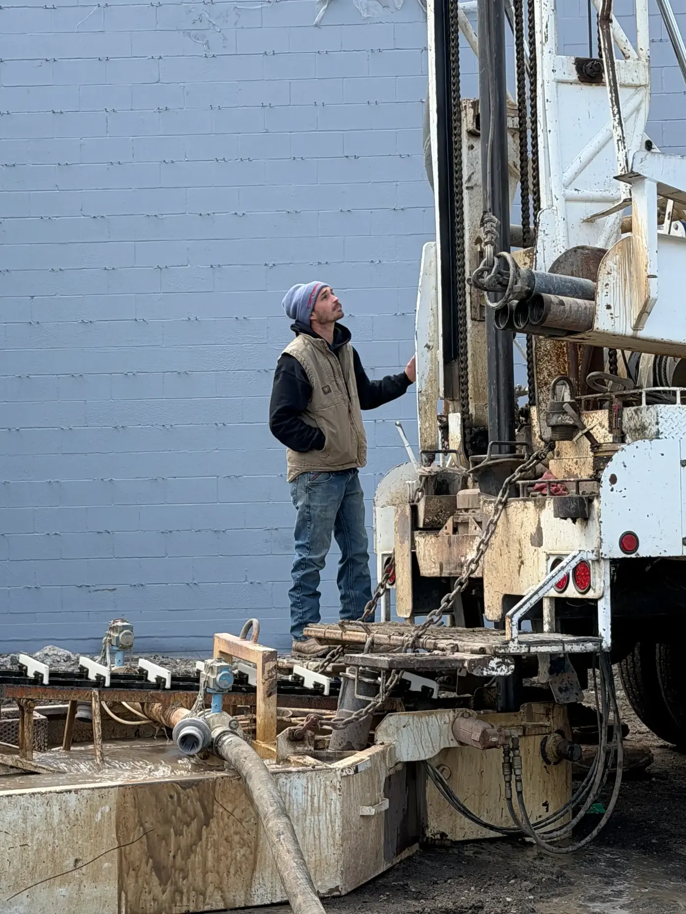 Chase Drilling LLC technician carefully lowering a new submersible water pump into a well casing at a Kansas residential property during a pump installation